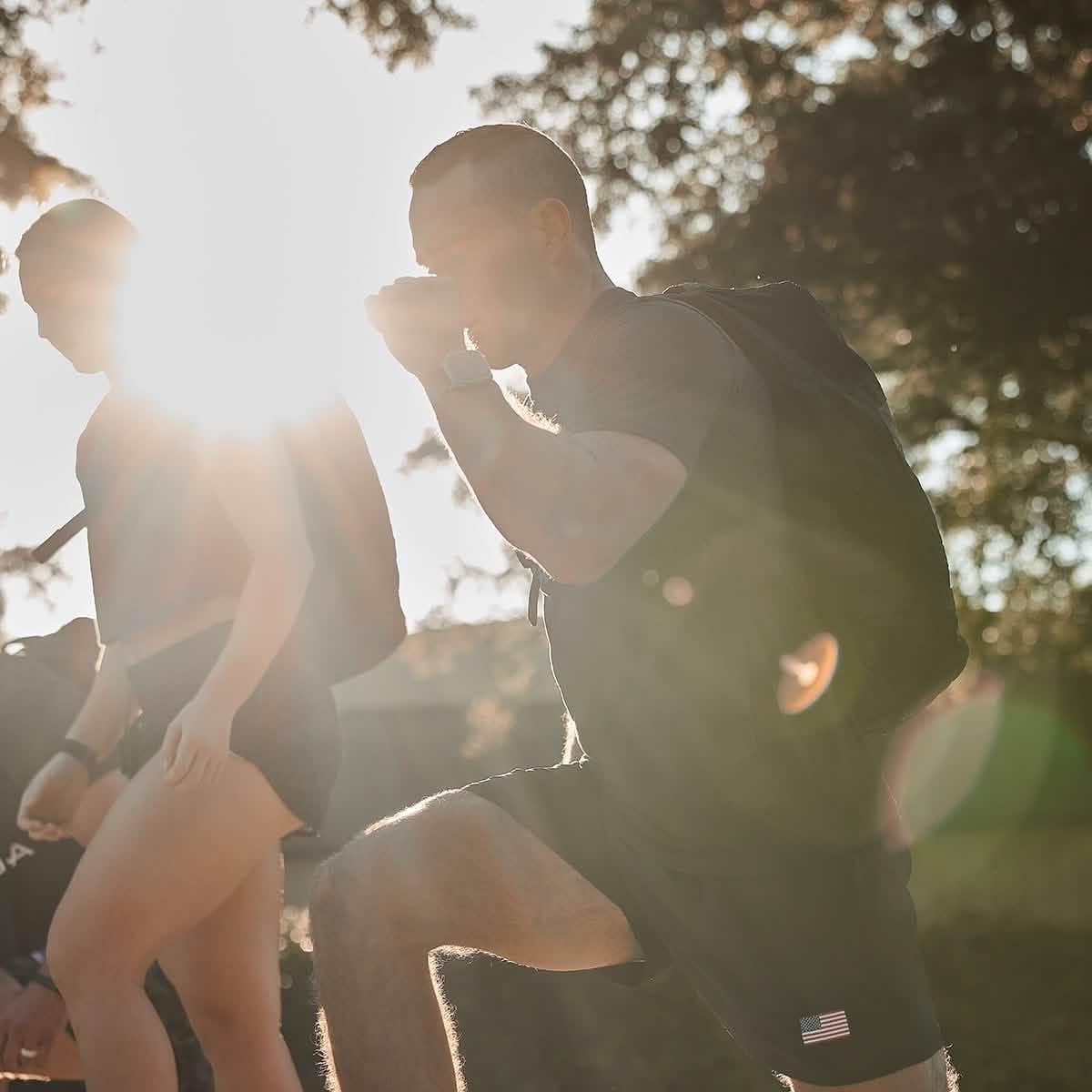 Two people wearing black USA training shorts and backpacks training outdoors with sun flare