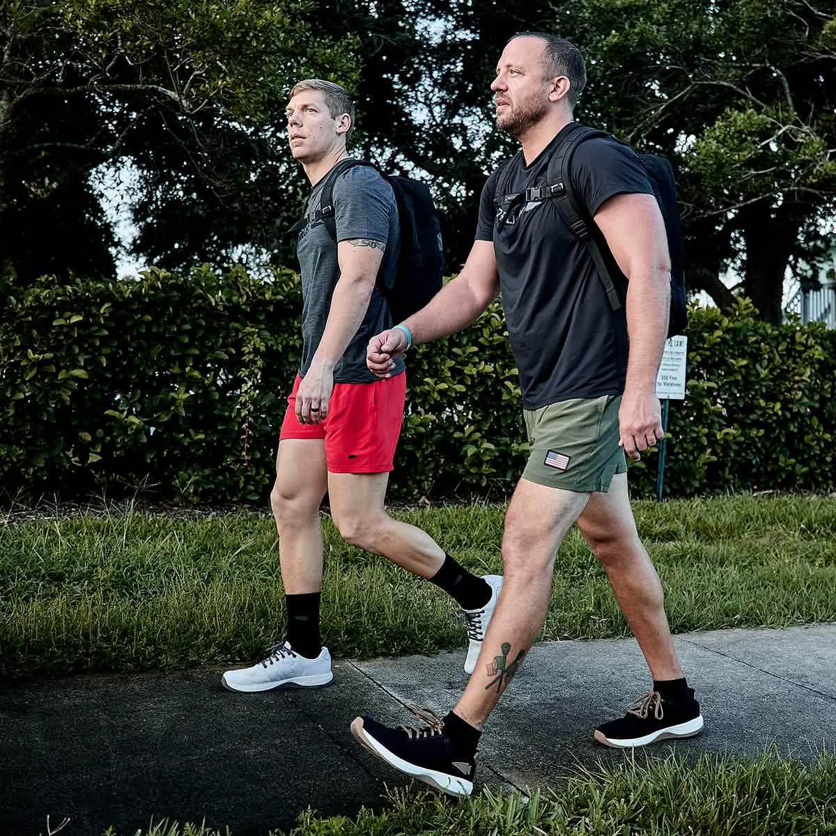 Two men wearing GORUCK training shorts and black t-shirts walking outdoors with backpacks