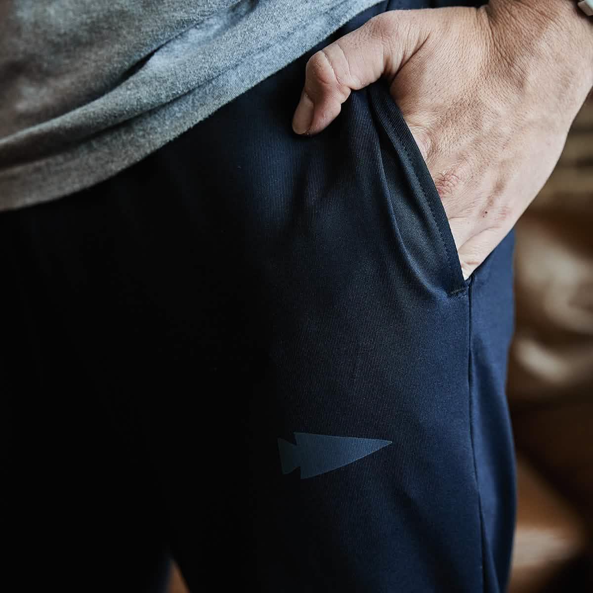 Close-up of a hand in pocket of black men's joggers with subtle arrow logo, casual athletic wear