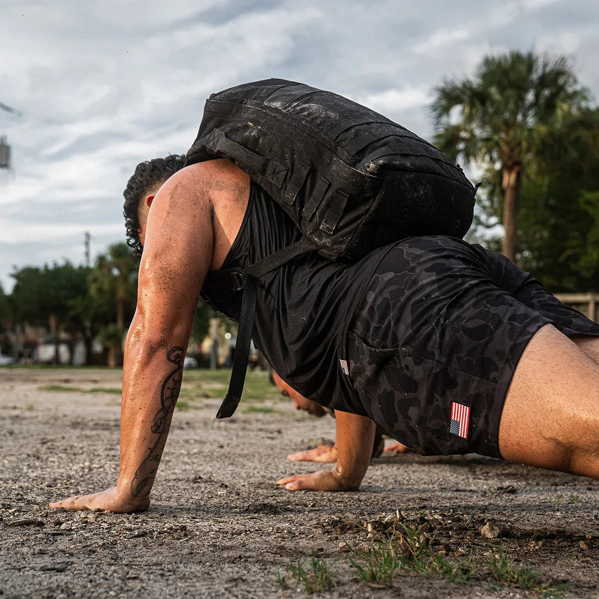 Man in black USA training shorts doing push-ups outdoors with a heavy black rucksack on back