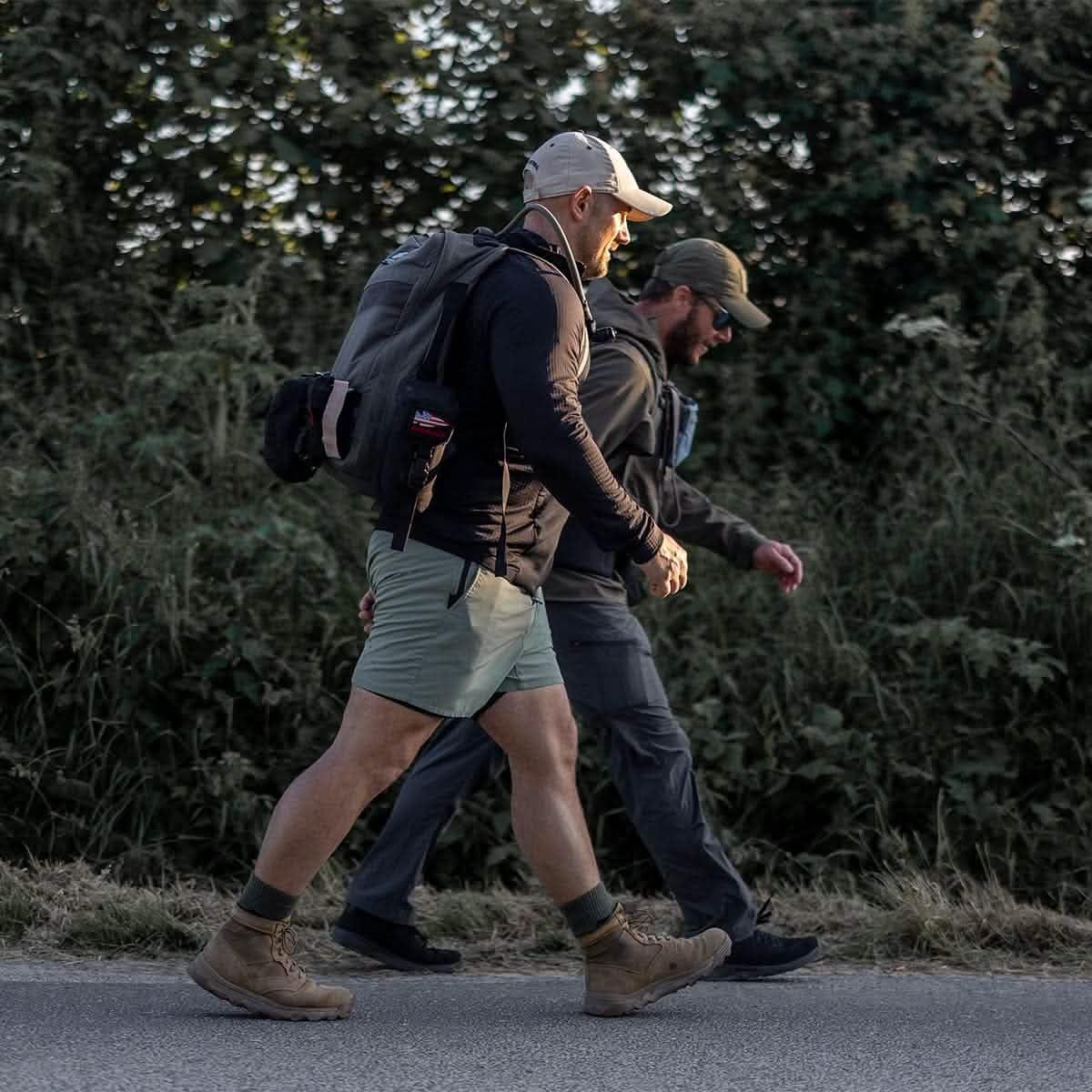 Two men rucking on a roadside in outdoor gear with backpacks during golden hour