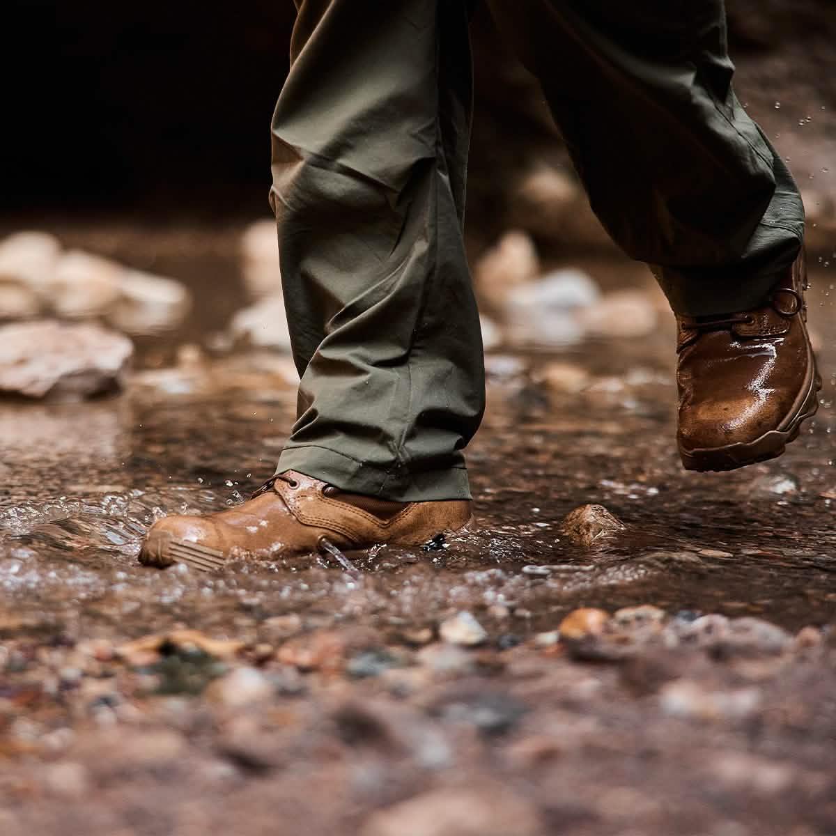 Close-up of hiker wearing waterproof brown boots and olive green pants splashing through rocky water
