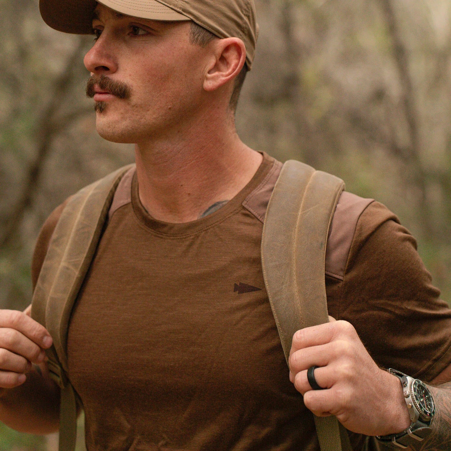 Man wearing GORUCK brown shirt and rucksack outdoors in rugged forest setting