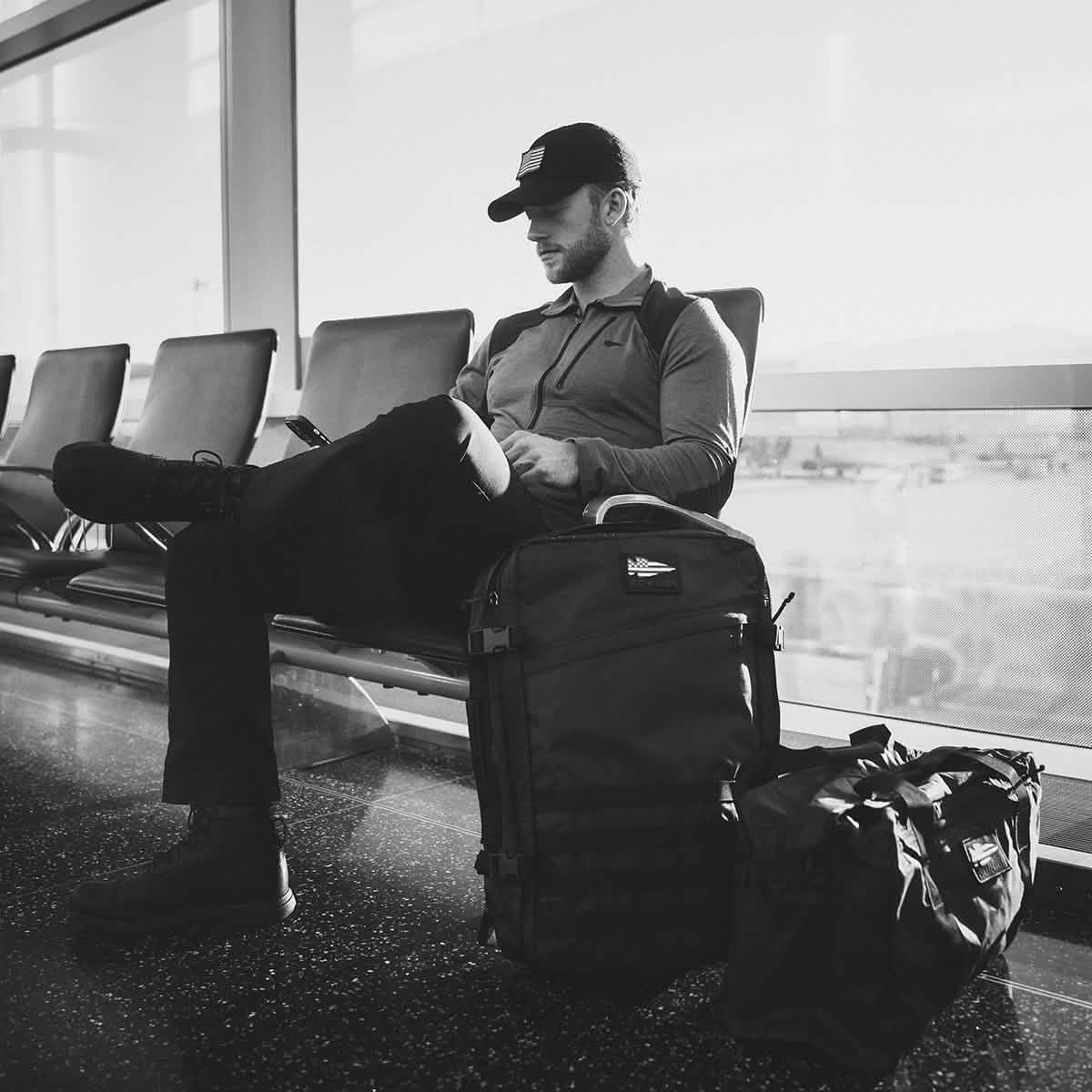 Man in casual outdoor gear sitting in airport seating with GORUCK black kitbag and duffel bag