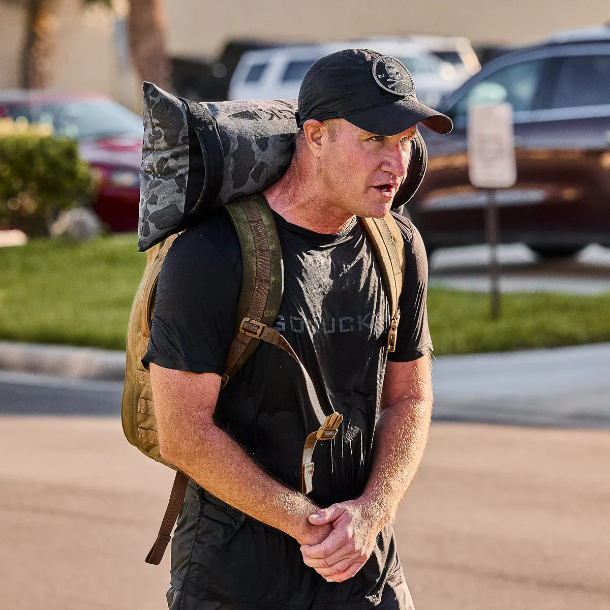 Man rucking outdoors with GORUCK gear, wearing black shirt, cap, and carrying weighted backpack