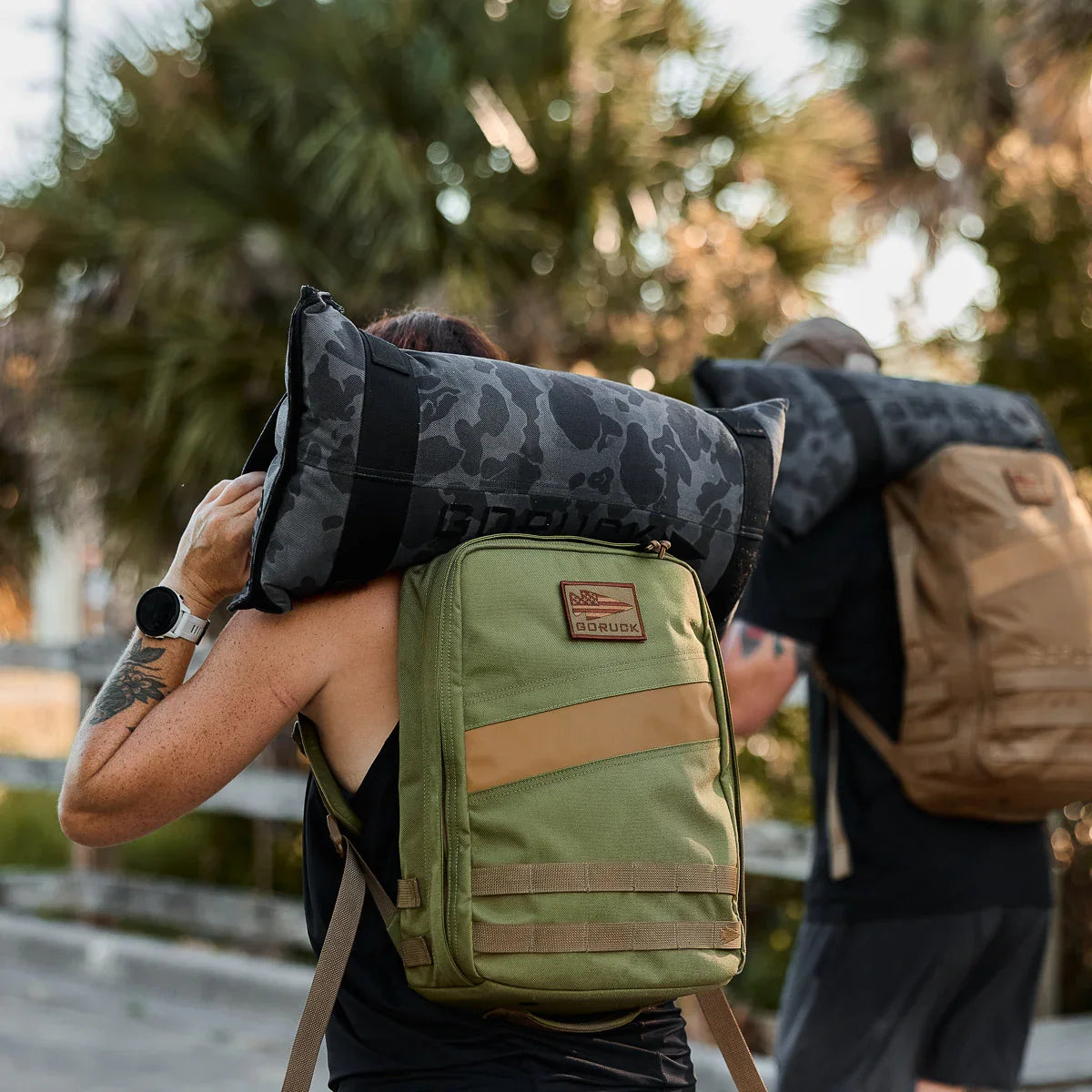 Two people rucking outdoors with GORUCK backpacks and camouflage sandbags