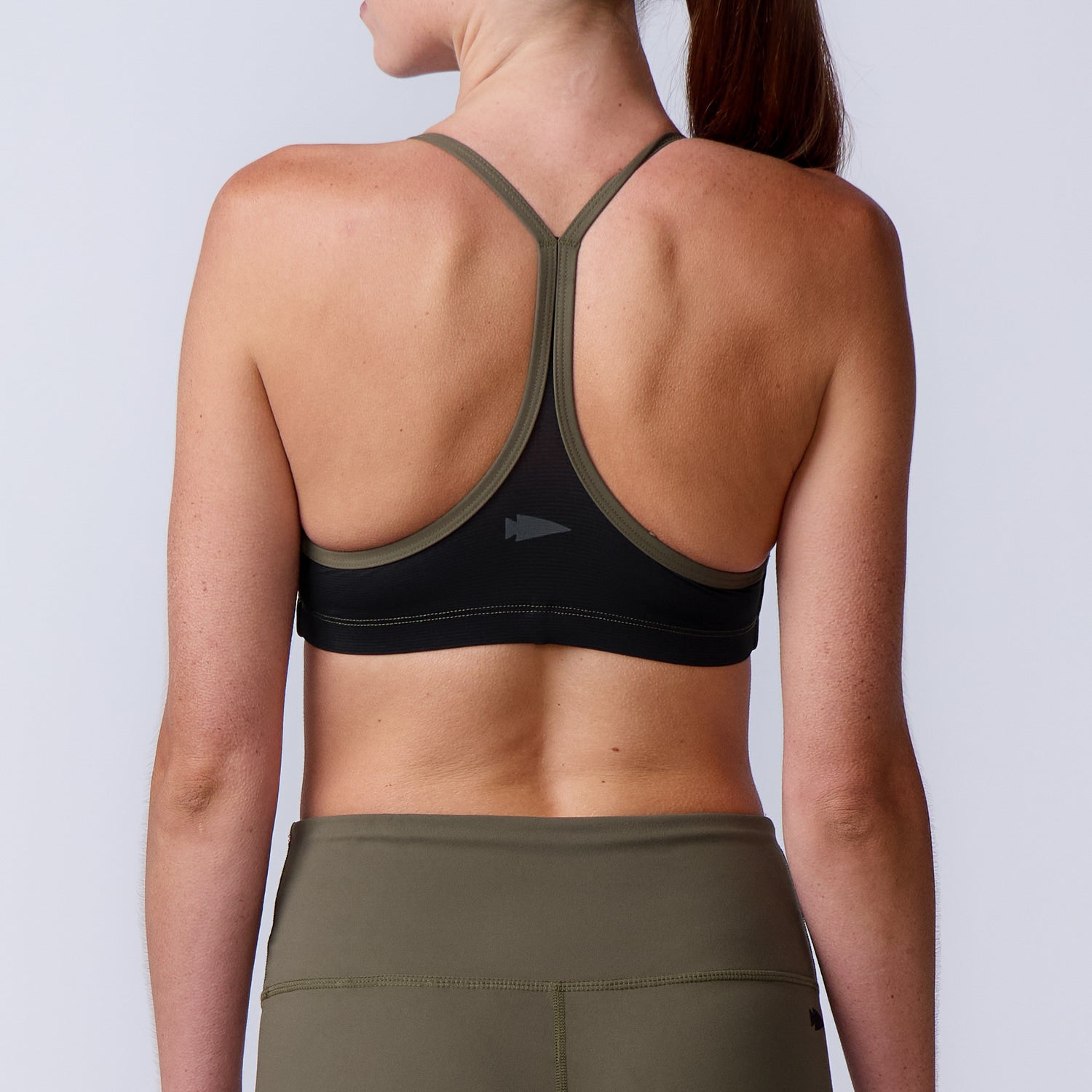 Woman wears the Stealth Bra - ToughFlex and olive leggings, shown from the back against a plain background. Lightweight support crafted with ToughFlex fabric for any workout.