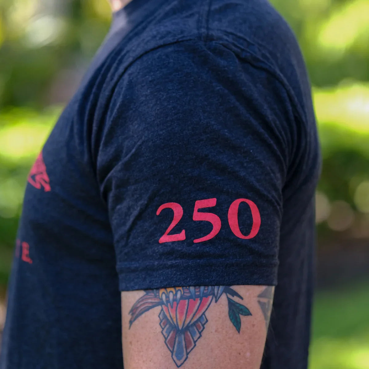 Close-up of person wearing black GORUCK t-shirt with red number 250 on sleeve and colorful tattoo on arm