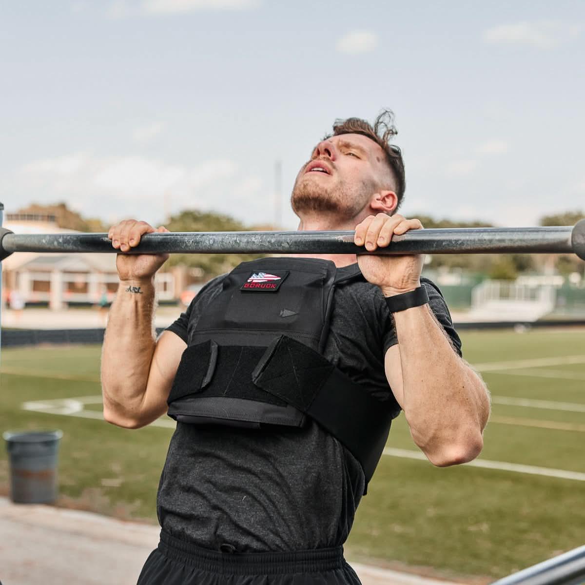 Man doing pull-up outdoors wearing GORUCK weighted vest, tough rucking fitness gear