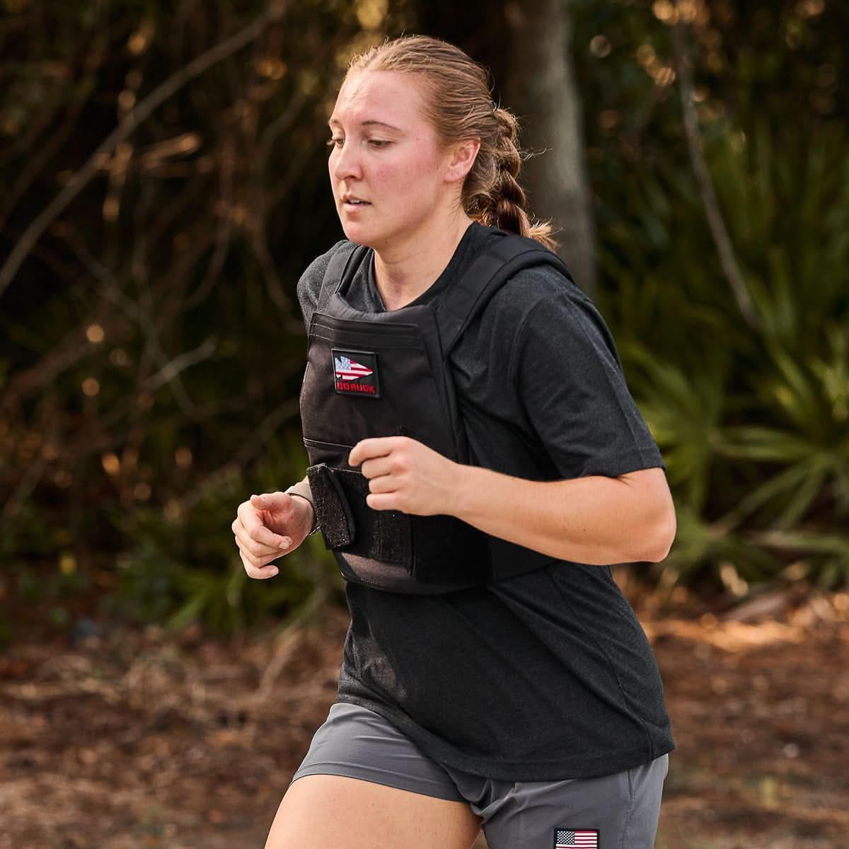 Woman running outdoors wearing GORUCK weighted vest and gray shorts with logo patch against natural background