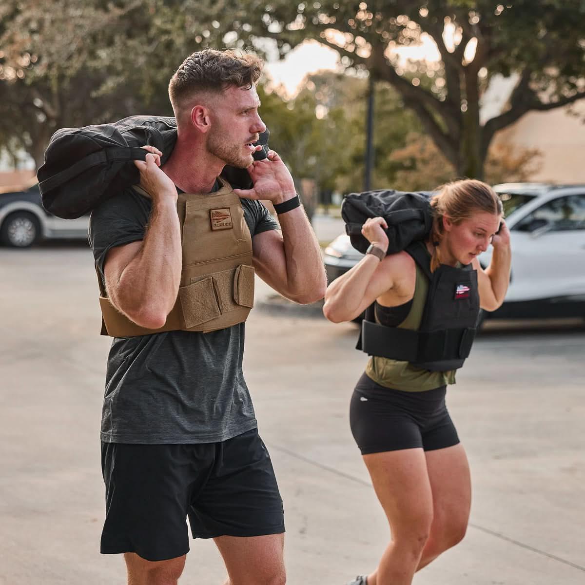 Man and woman rucking outdoors in GORUCK weighted vests carrying sandbags