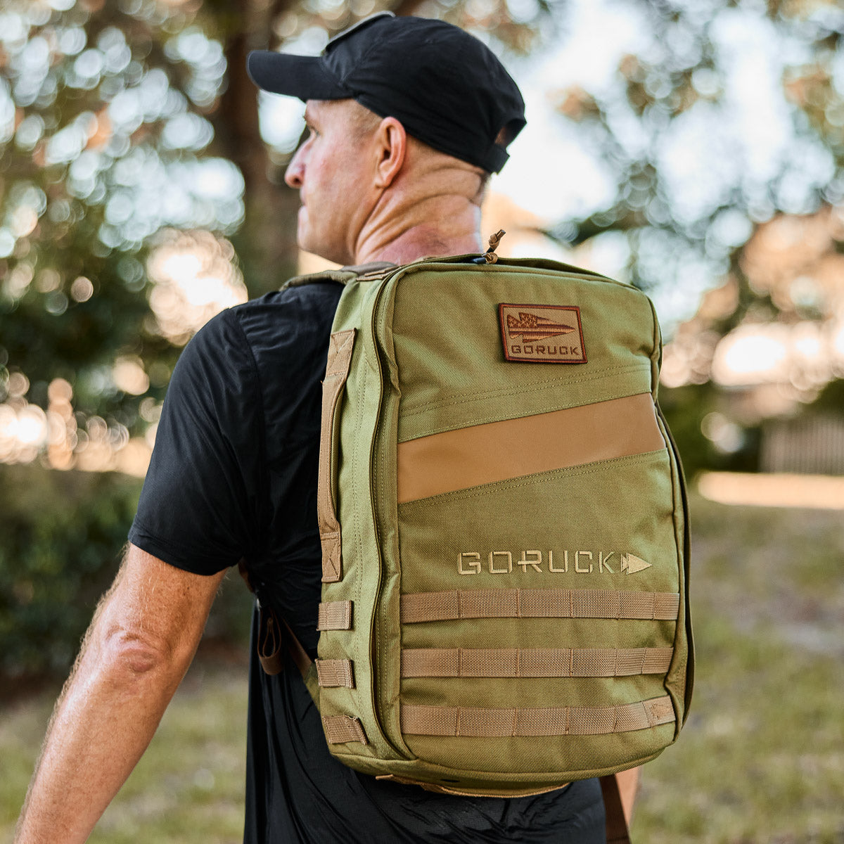 Man outdoors wearing a black cap and shirt, carrying the Rucker 4.0 backpack in green on his back.