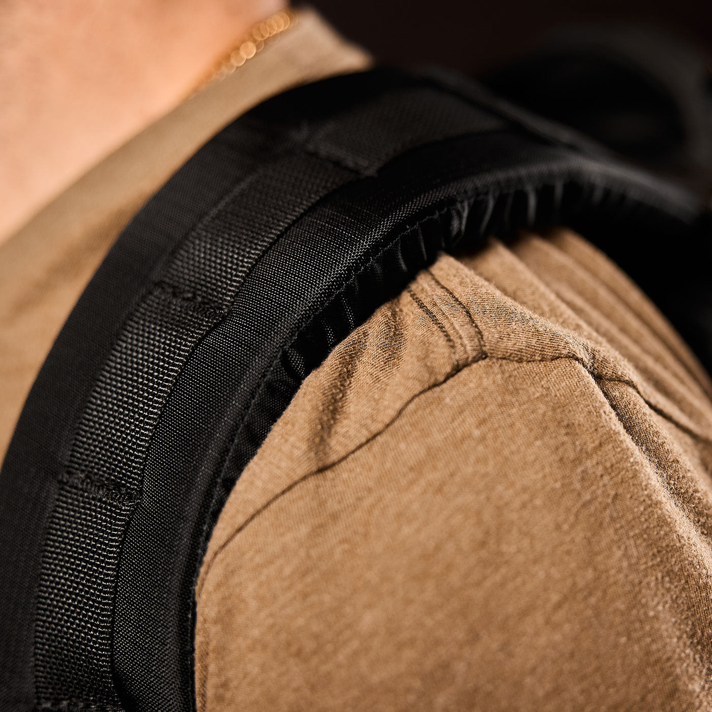 Close-up of a person wearing a tan shirt and a black backpack strap over their shoulder.