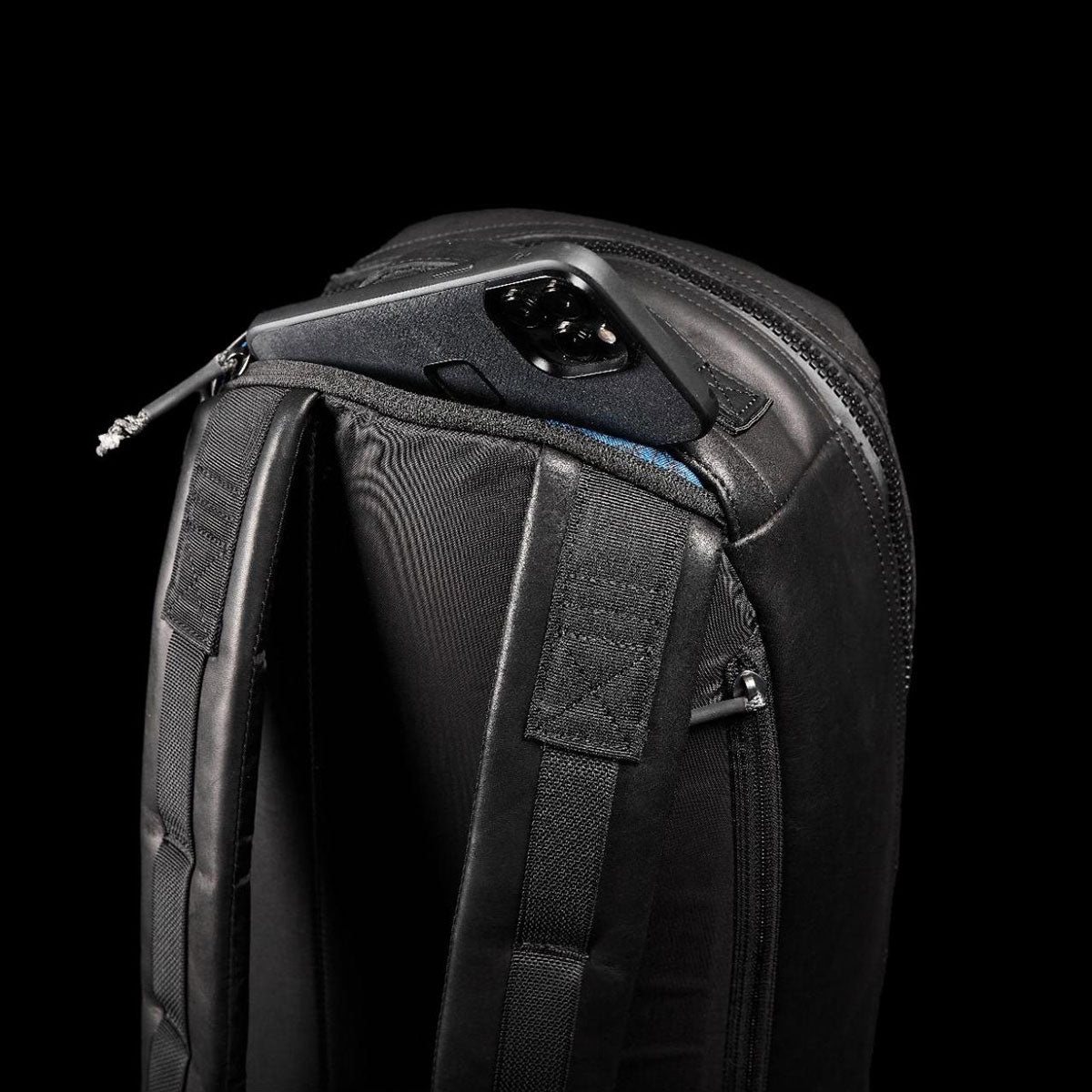 Black backpack with a hidden zipper pocket holding a black smartphone against a black background.