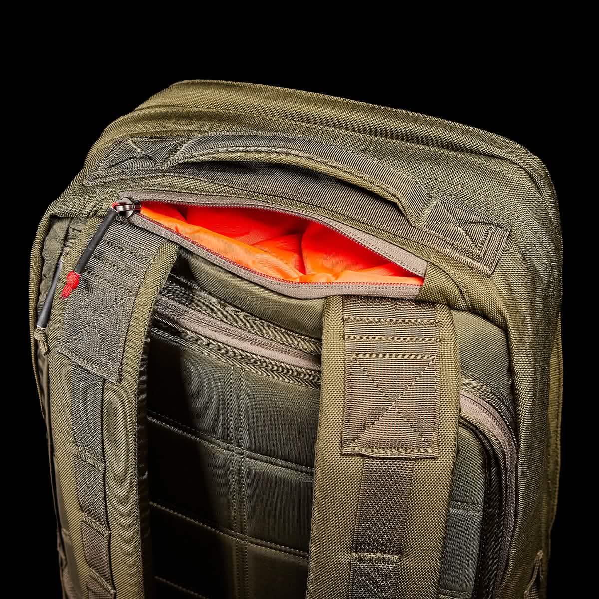 Close-up of an olive green ruck resembling the durable GORUCK GR2 - Cordura model, boasting a vibrant orange interior. It features padded shoulder straps and a partially open top zipper. The ruck appears sturdy with reinforced seams, set against a bold black background, mirroring Special Forces reliability.