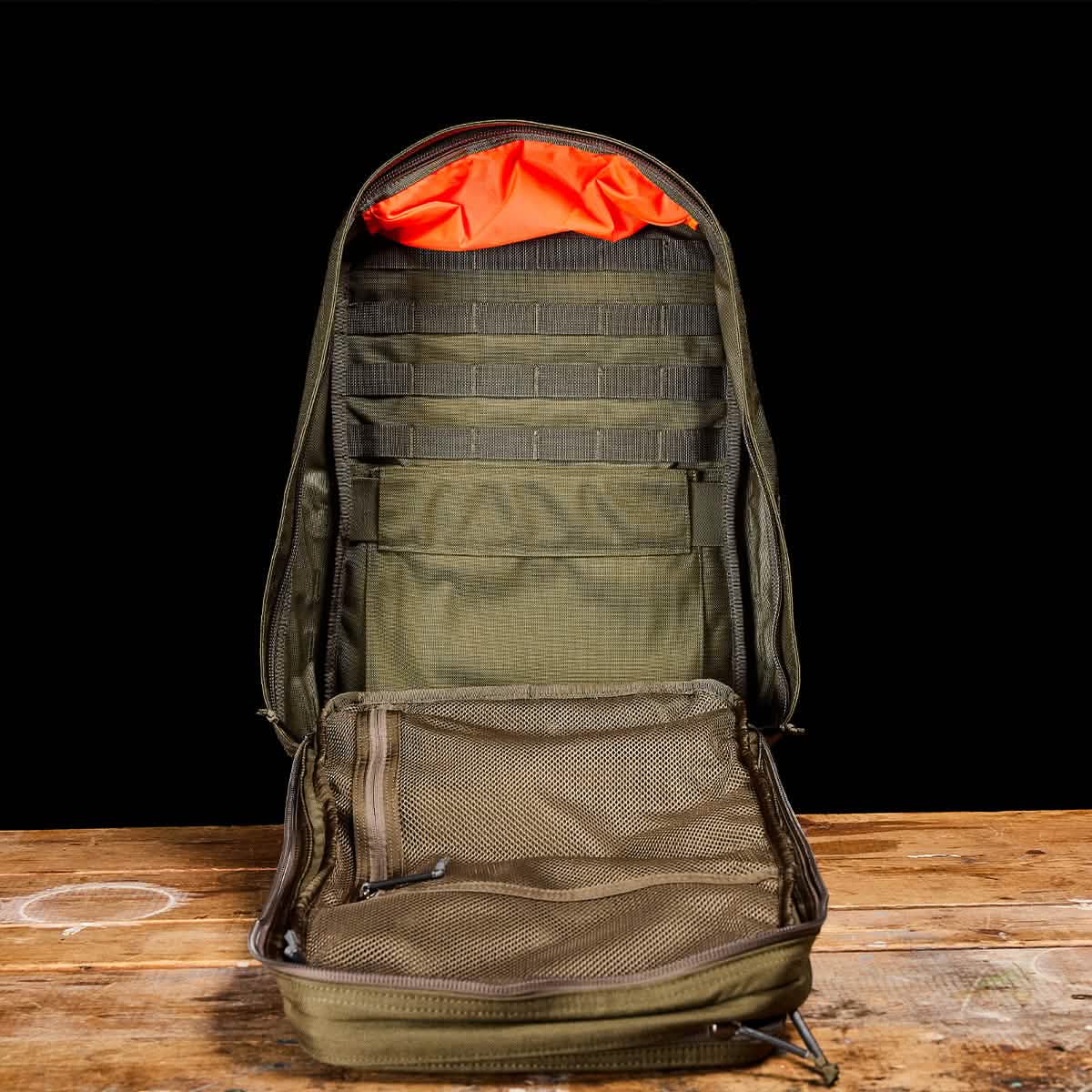 Open Ranger Green GORUCK backpack showing MOLLE straps, mesh pockets, and bright orange interior lining