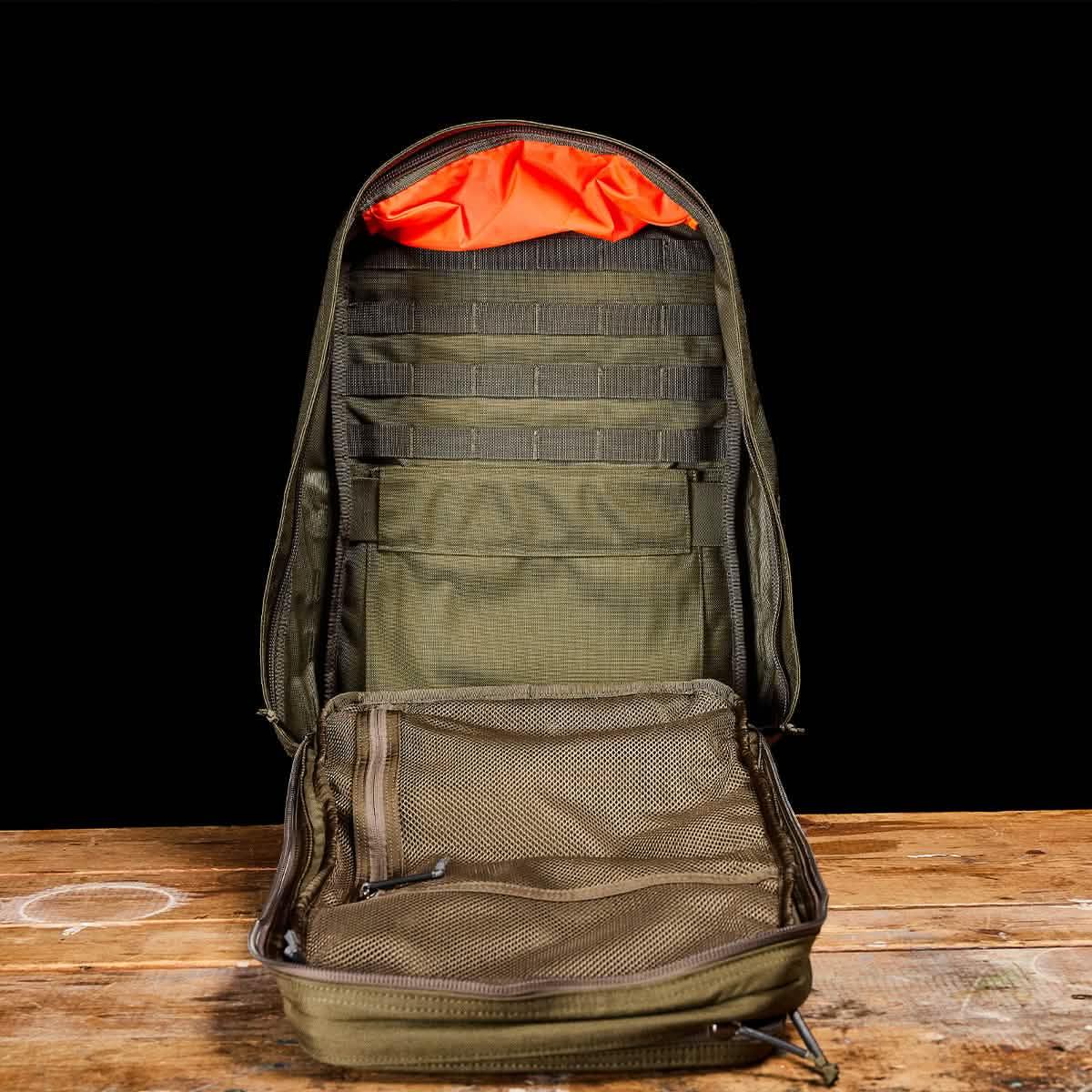 Open Ranger Green GORUCK backpack showing MOLLE straps, mesh pockets, and bright orange interior lining