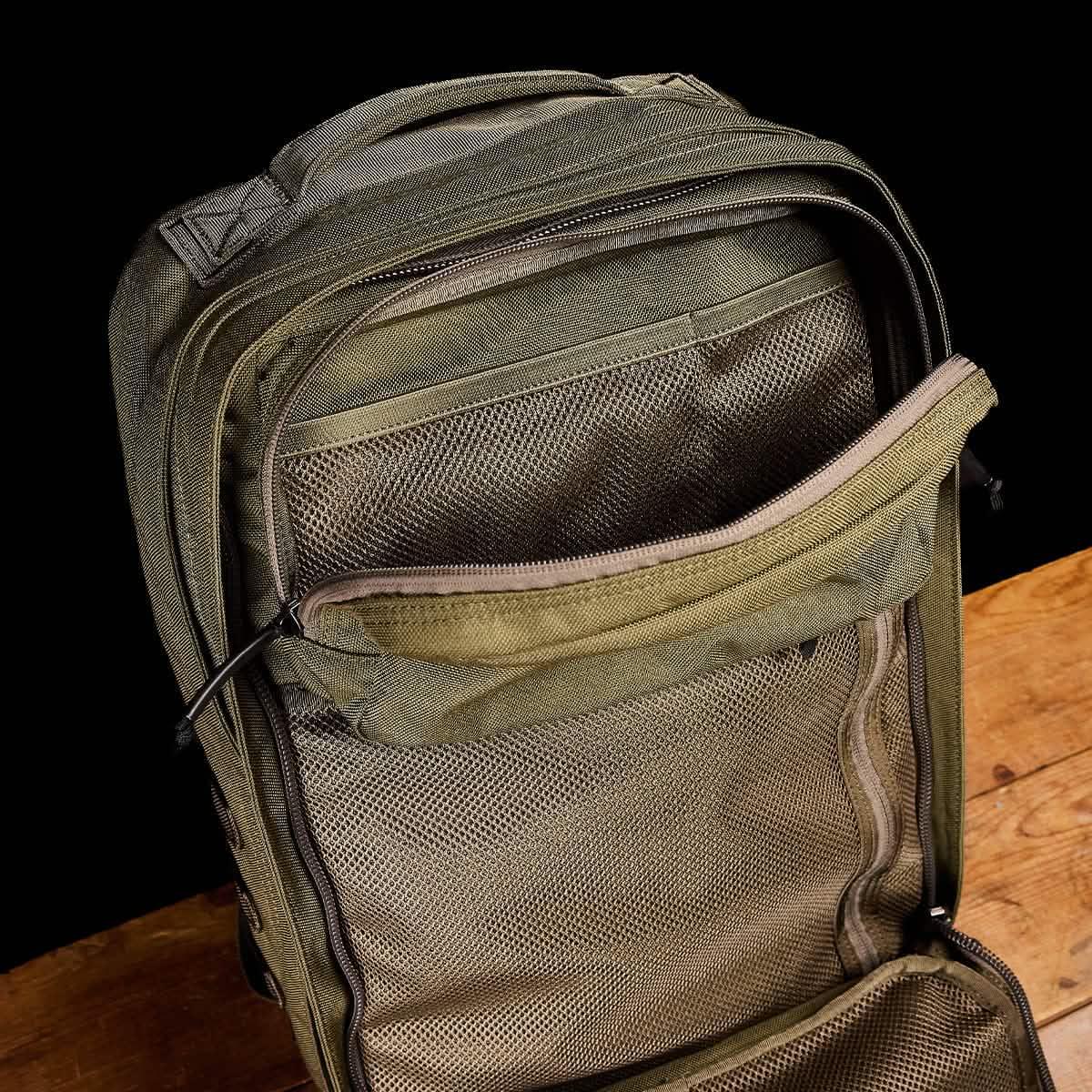 Open ranger green GORUCK backpack showing internal mesh pockets and durable zippers on wooden surface