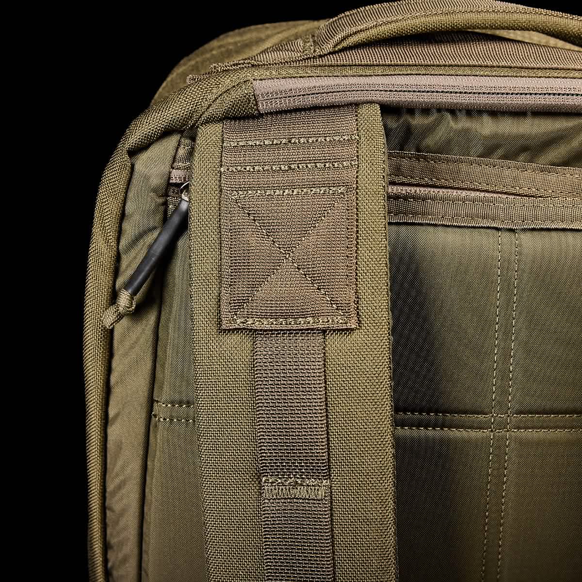 A close-up of the GR2 backpack strap and upper section in olive green against a black background. The strap, featuring detailed stitching and a plastic loop, reflects GORUCK's Special Forces quality. The fabric texture is visible, highlighting its durable material.