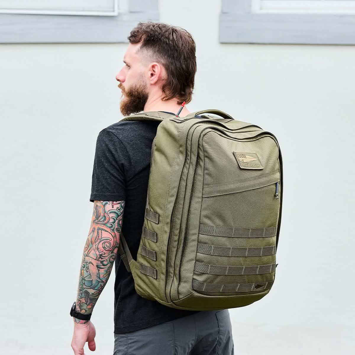Man with beard and tattoo wearing a black shirt and carrying a large ranger green GORUCK tactical backpack