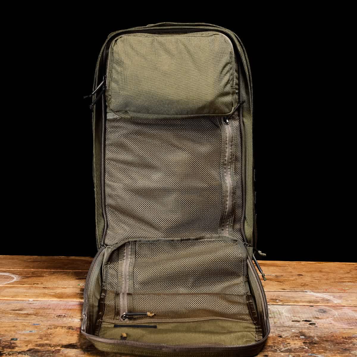 An open GR2 - Cordura backpack in a green color, featuring multiple mesh compartments, is showcased on a wooden surface against a black background, showcasing the rugged functionality of a GORUCK Special Forces ruck.