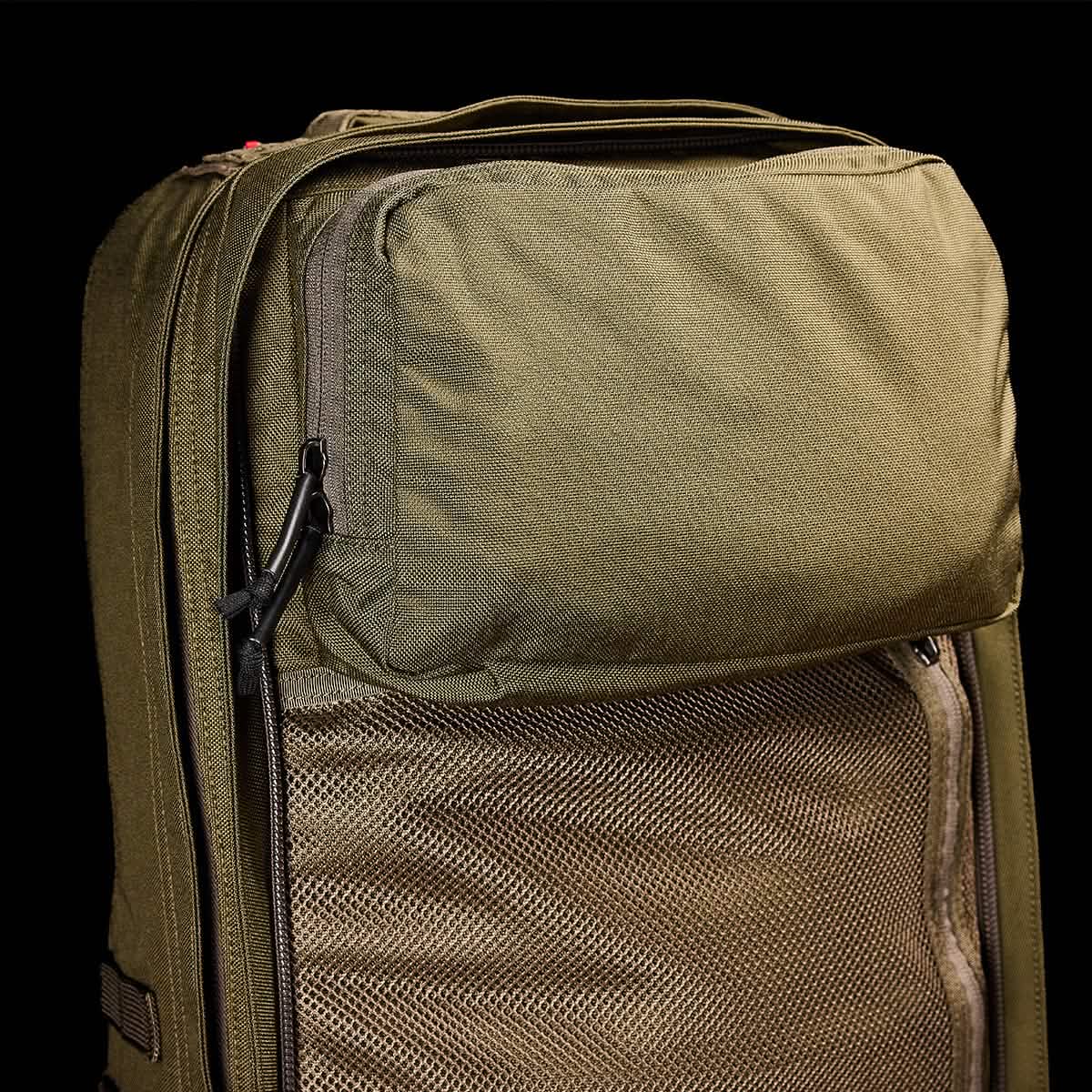 Close-up of a green GR2 - Cordura by GORUCK against a black background. This Special Forces-inspired backpack features a large front pocket with a zipper, mesh panel detailing, and appears to have durable fabric.