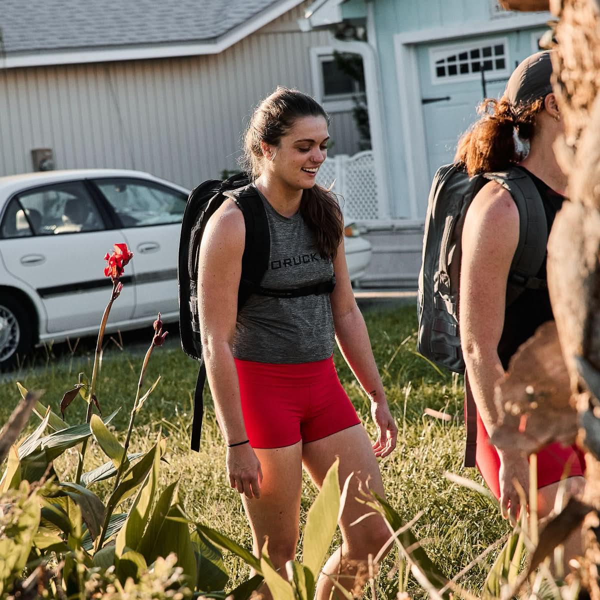 Women rucking outdoors wearing GORUCK gear and red squat shorts in a grassy yard