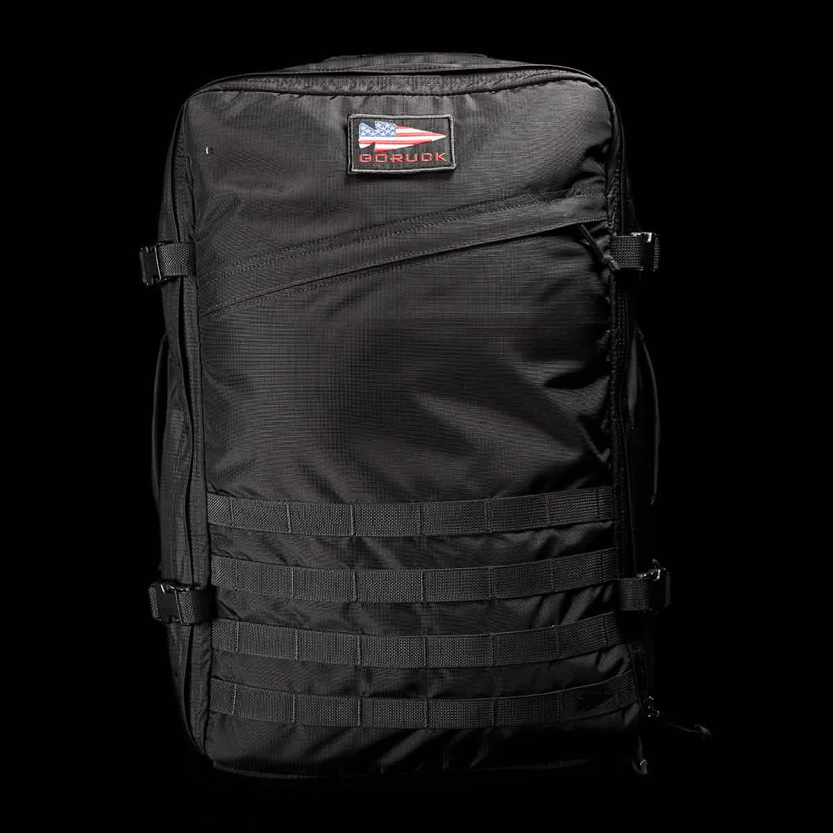 The GR3 - Ripstop ROBIC® by GORUCK, made from sturdy Robic nylon, features numerous compartments and straps against a dark backdrop. This ideal carry-on rucksack highlights the iconic GR3 design along with a logo displaying an American flag motif.