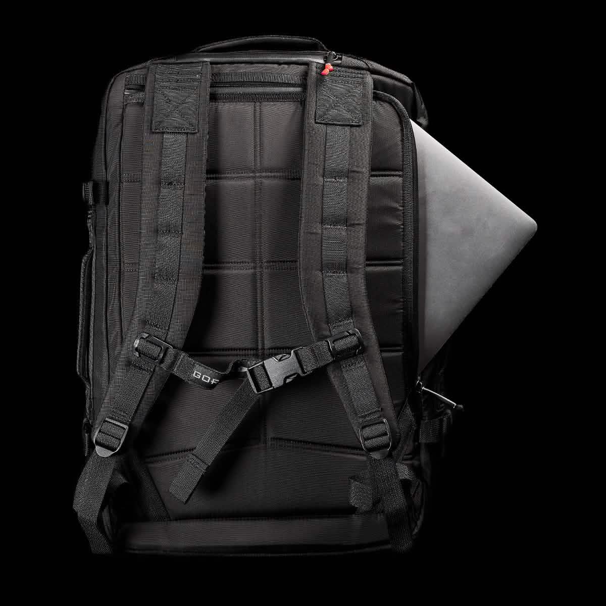 The GR3 - Ripstop ROBIC® carry-on rucksack from GORUCK is showcased from the back against a black background, highlighting its durable ROBIC nylon construction. Visible features include the straps, padding, and a small pocket. A sleek laptop is partially tucked into one of the compartments, emphasizing the rucksack's tech-friendly design.