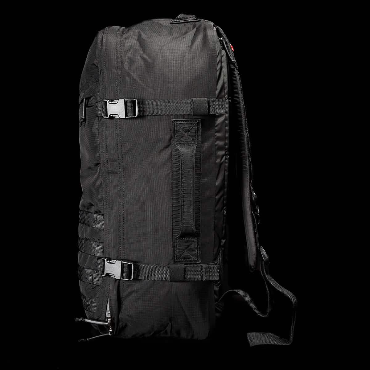 A GR3 - Ripstop ROBIC® backpack from GORUCK is showcased sideways against a black background. Made from rugged Robic nylon, it includes adjustable straps, buckles, and a top handle. Its minimalist design emphasizes its practicality as a carry-on rucksack.