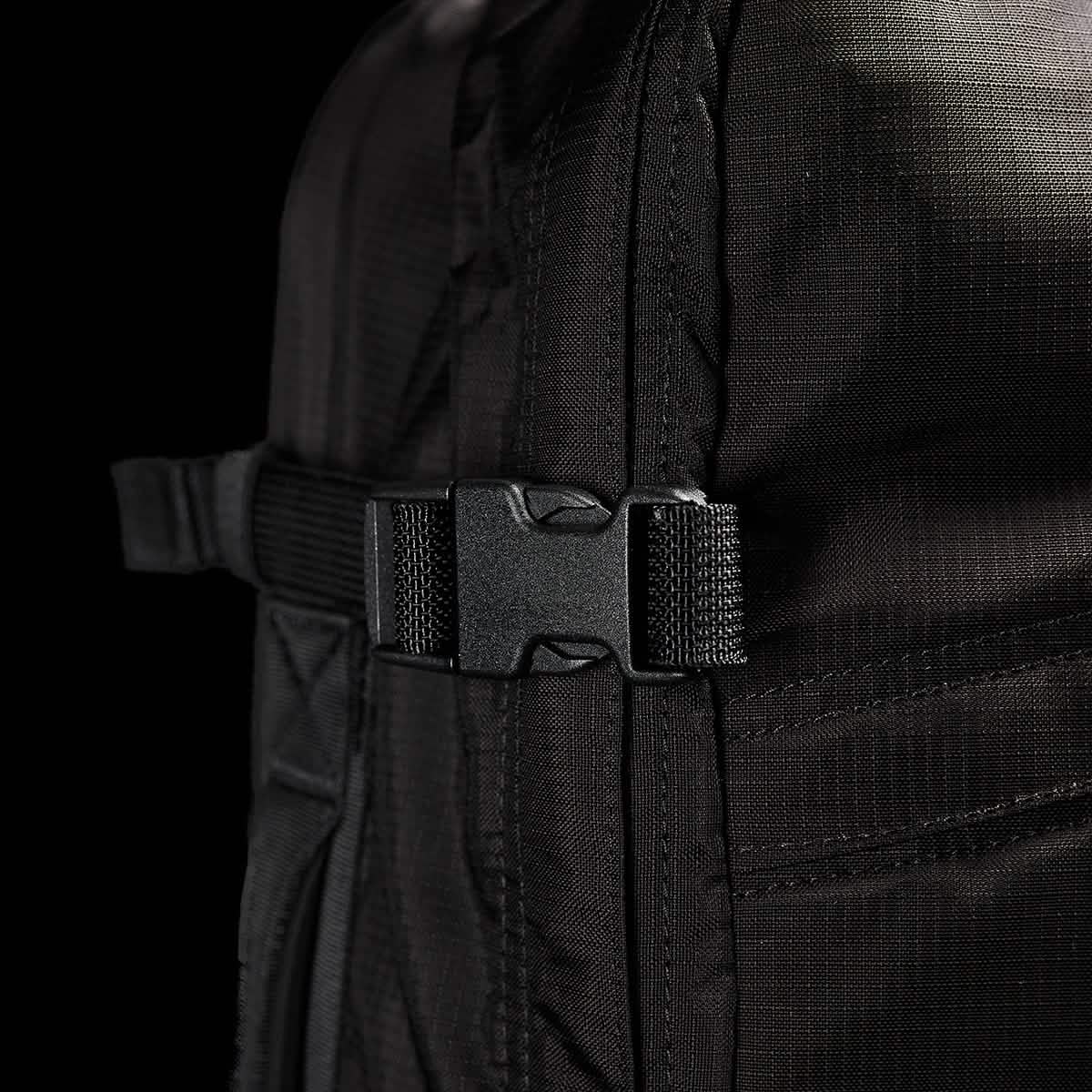 A close-up of a black GORUCK GR3 - Ripstop ROBIC® carry-on rucksack highlights its sturdy side buckle and strap. The texture of the ROBIC® nylon fabric showcases its durability and robust design, set against a dark background that accentuates the backpack’s standout features.