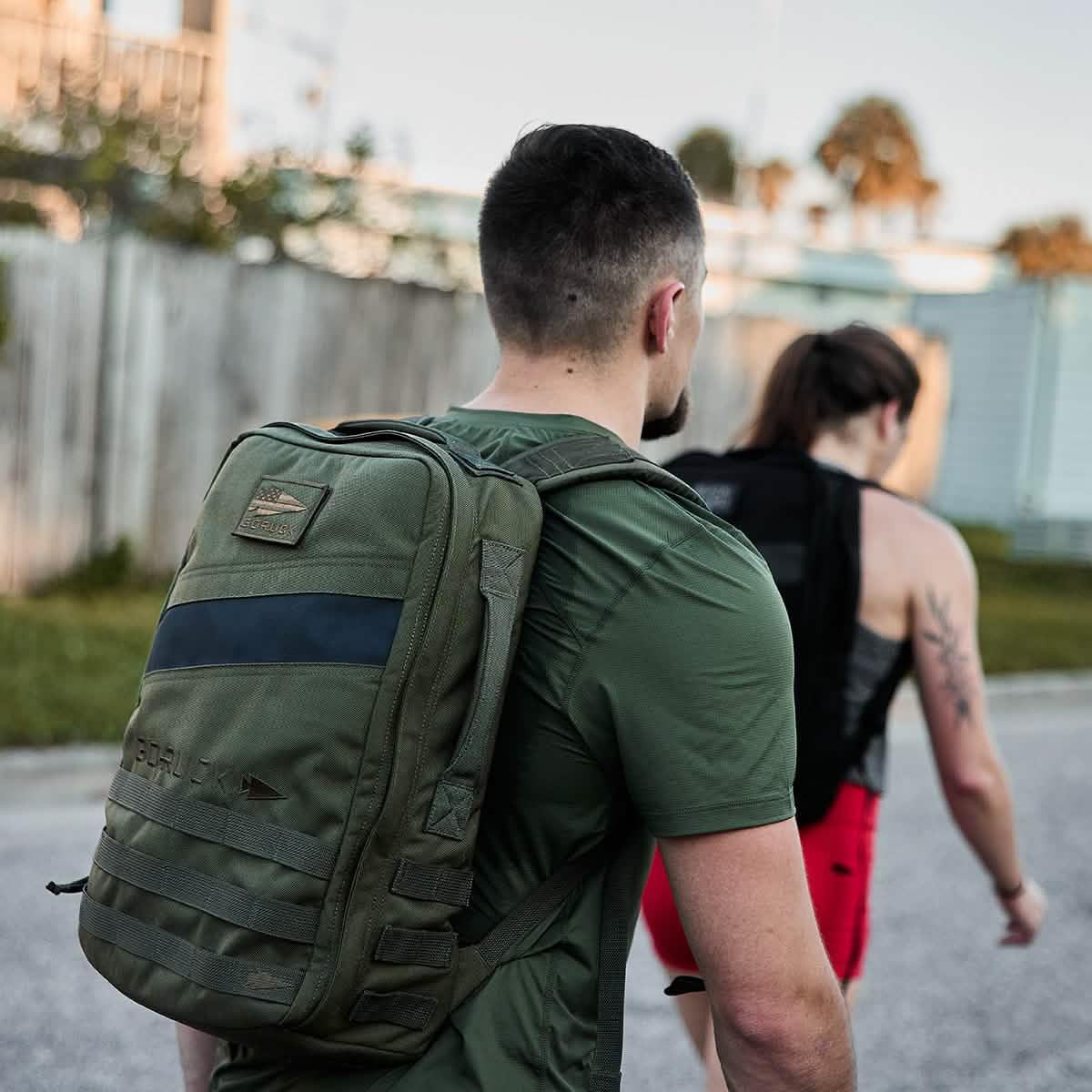 Man wearing green GORUCK Rucker 20L backpack with woman walking ahead outdoors