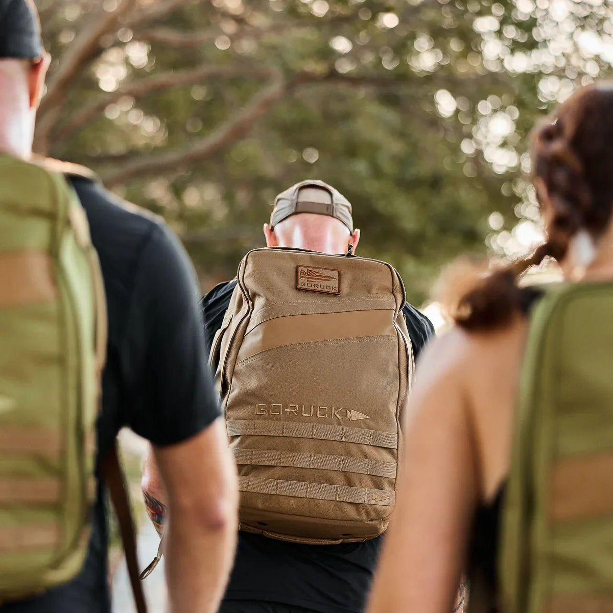 Group of people outdoors wearing GORUCK rucksacks, featuring the tan Rucker 4.0 25L backpack in center
