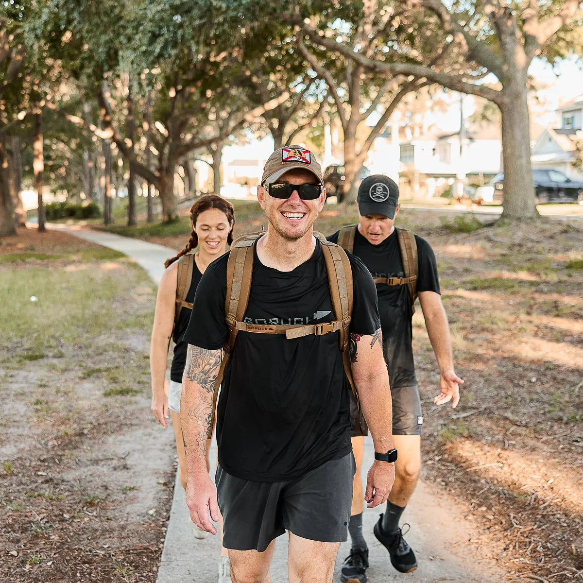 Three happy people rucking outdoors on a tree-lined path wearing GORUCK gear and backpacks