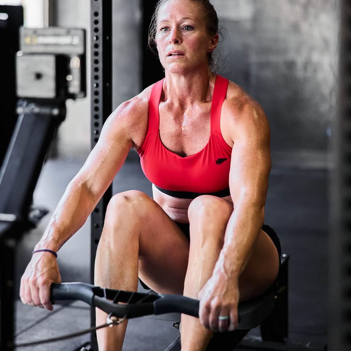Athletic woman in red sports bra using rowing machine in gym workout, focused and sweaty