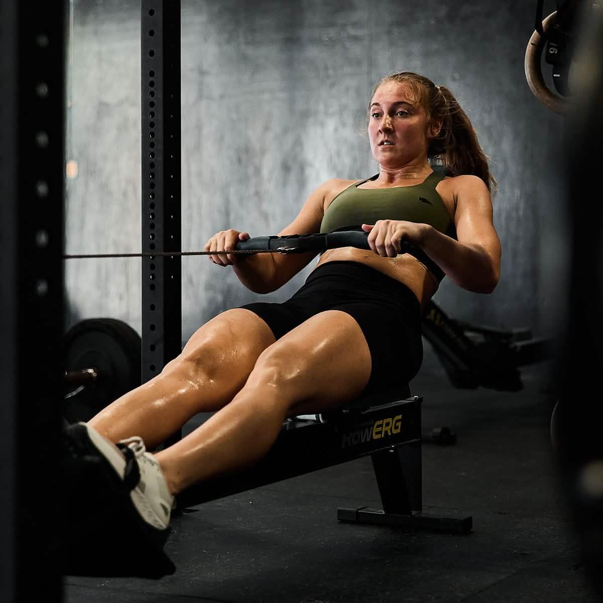 Athletic woman in green sports bra rowing on a rowing machine in a gym setting