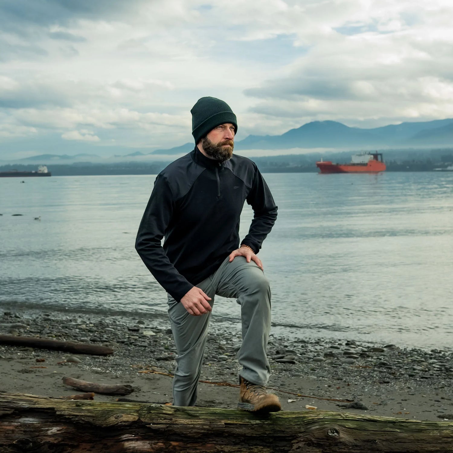 Man in GORUCK outdoor apparel rucking on rocky lakeshore with ship and mountains in background