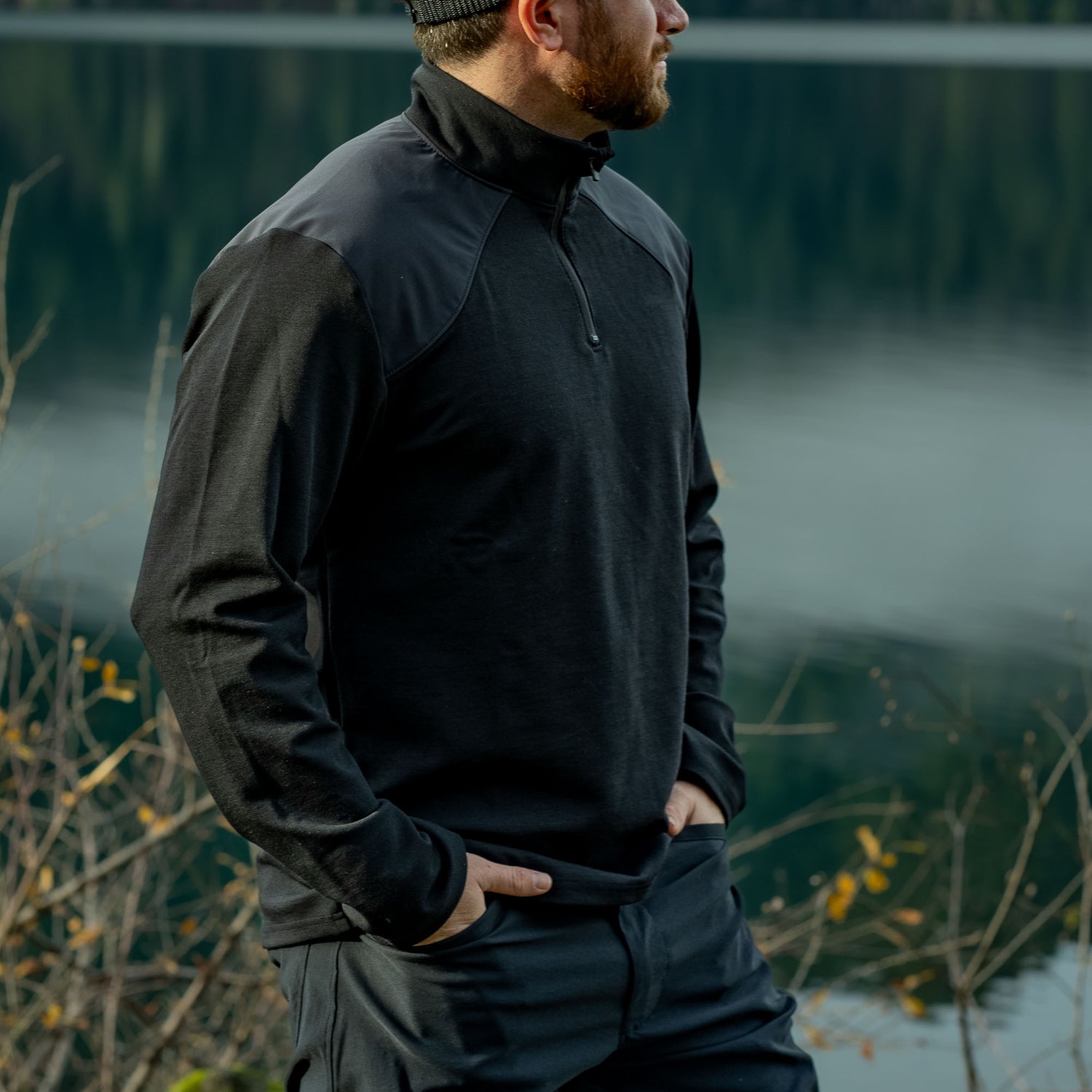 Man wearing GORUCK black quarter-zip rucking jacket outdoors near a lake