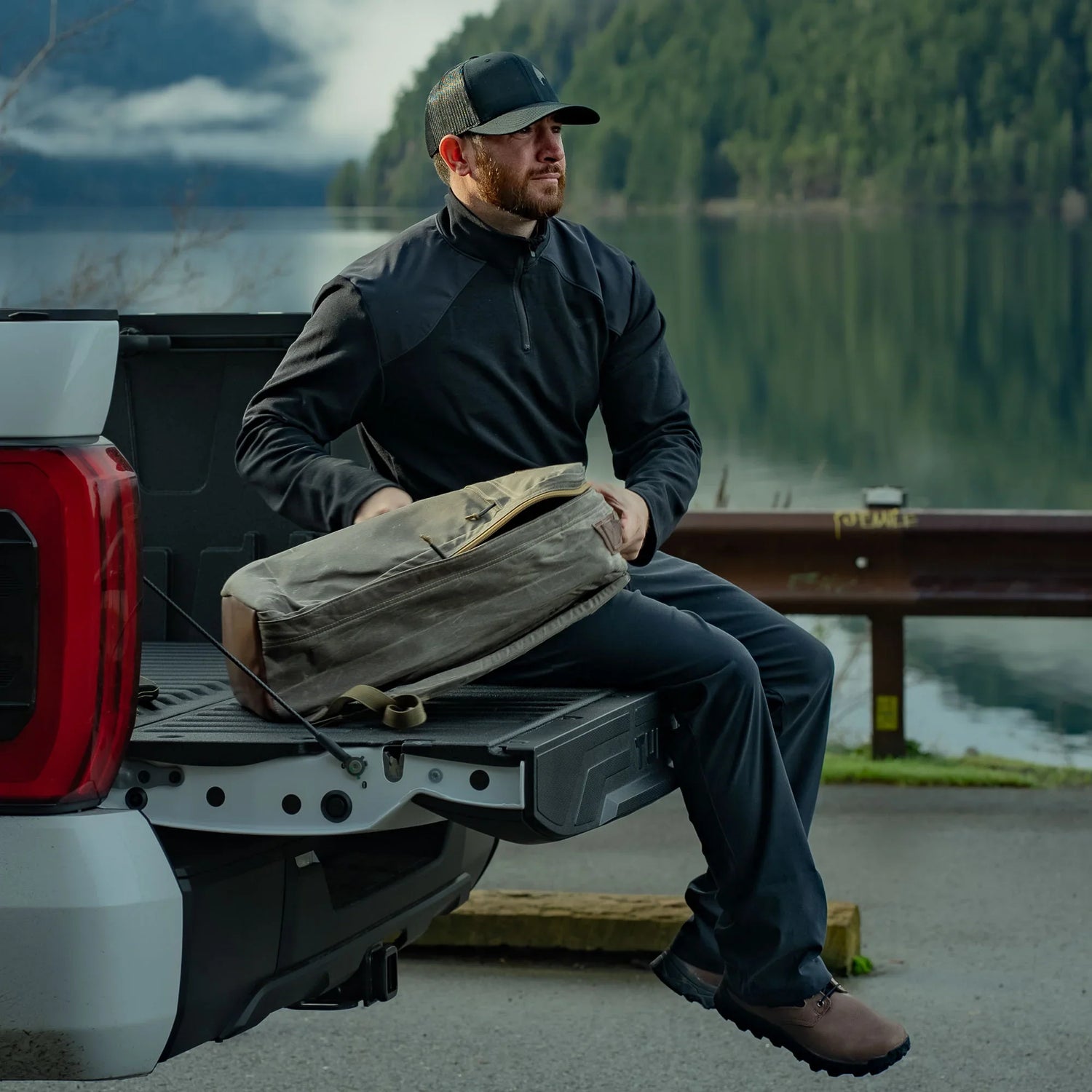 Man sitting on truck tailgate by lake with GORUCK rucksack, outdoor adventure gear