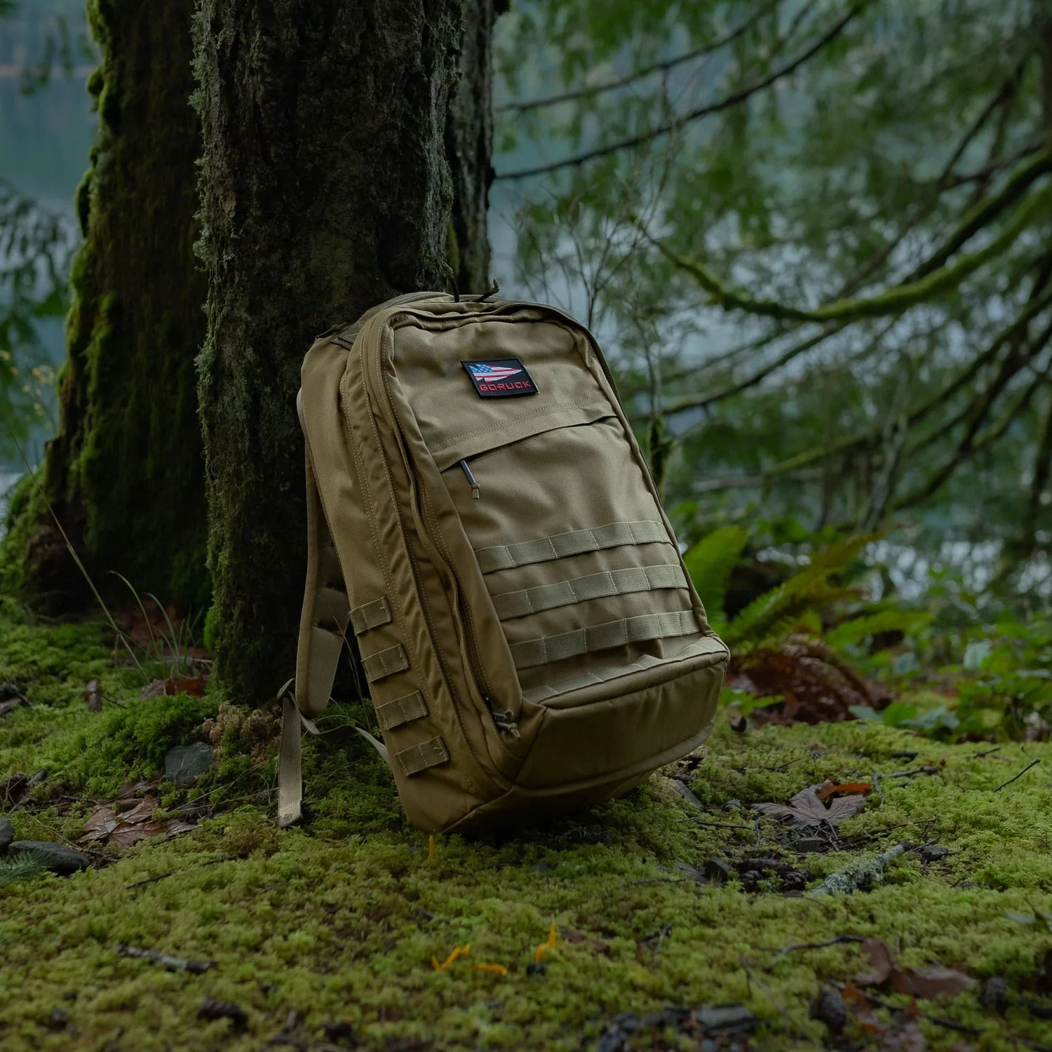 GORUCK tactical backpack resting on mossy forest ground near a tree, outdoor rucking gear