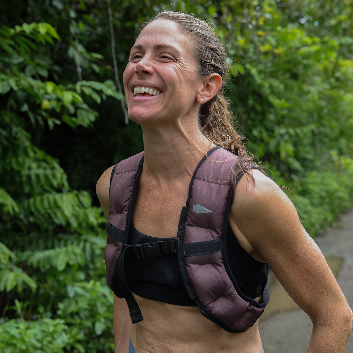 A woman in athletic wear smiles on a wooded trail while carrying the stylish Spy Ruck backpack.