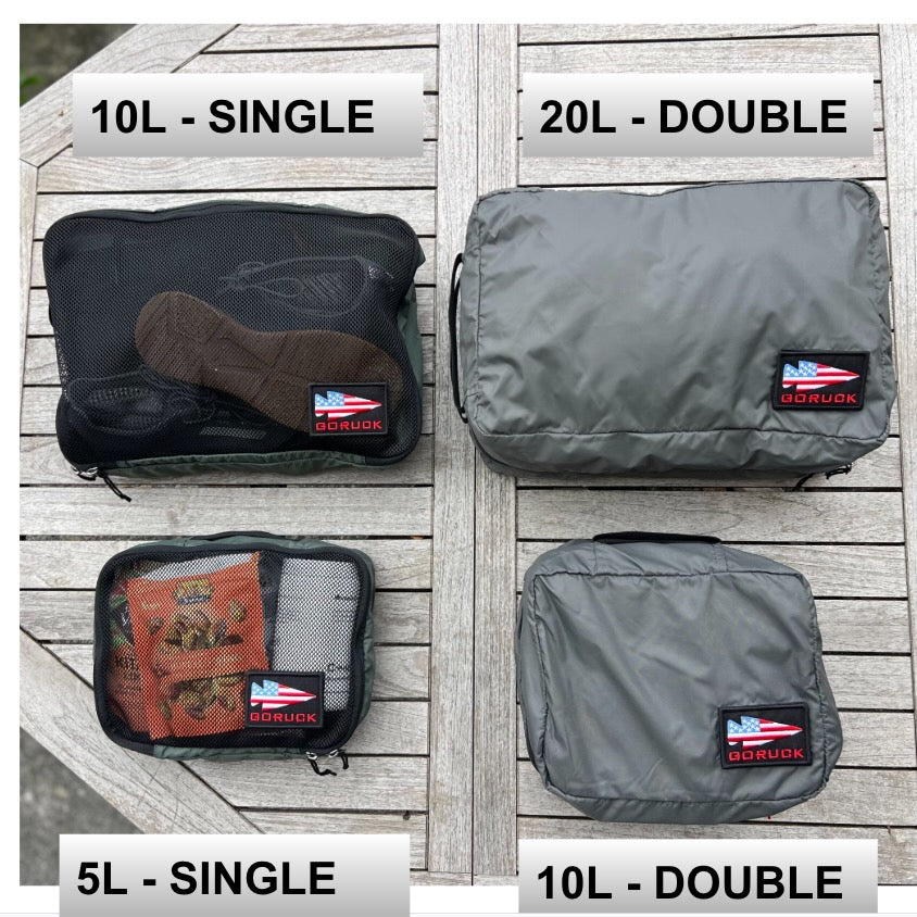 Four ultra-light nylon GORUCK packing cubes arranged on a wooden surface: a 10L single-compartment cube, a 20L double-compartment cube, a 5L single-compartment cube, and a 10L double-compartment cube for travel organization.