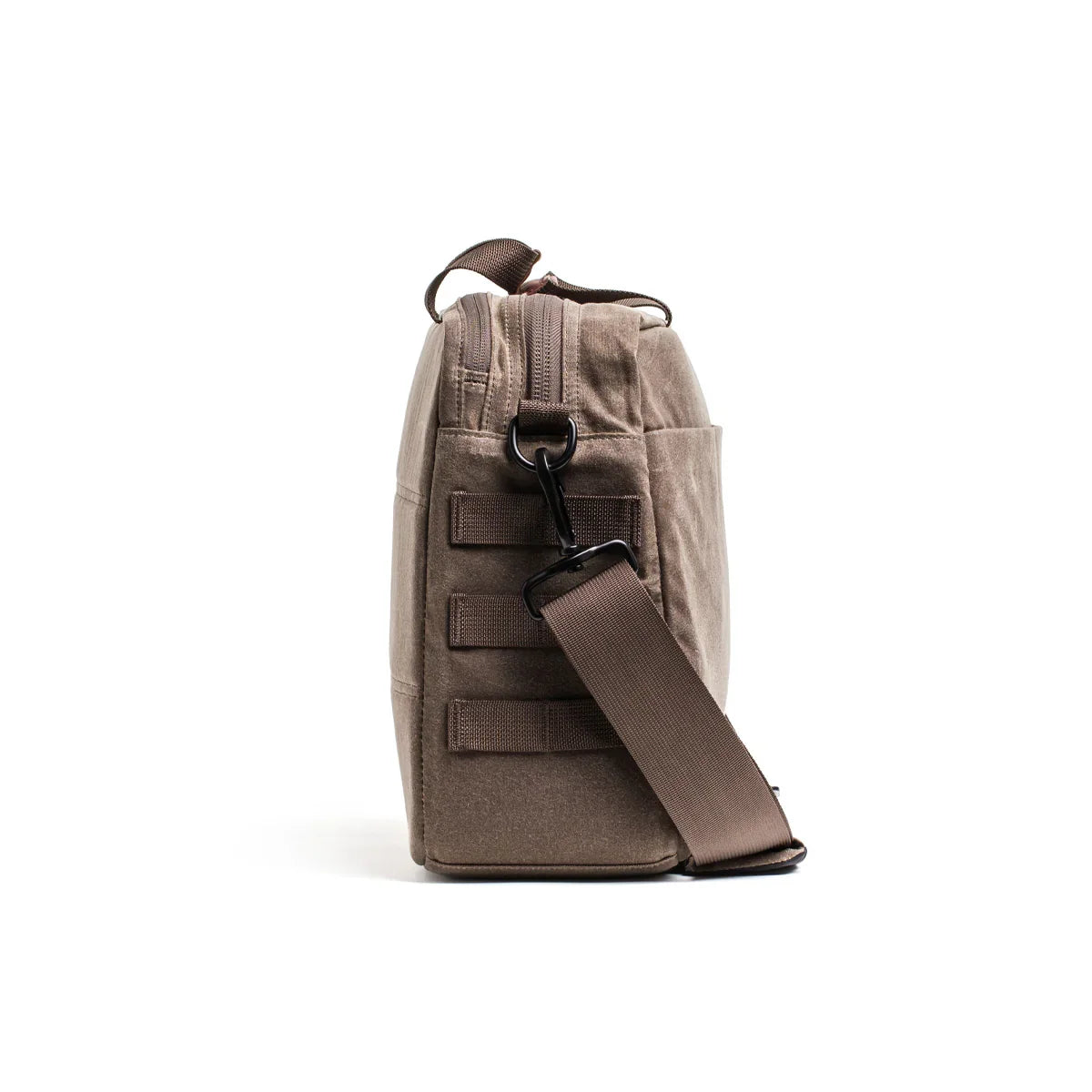 Side view of a dark oak waxed canvas shoulder bag with adjustable strap and stitched loops on white background