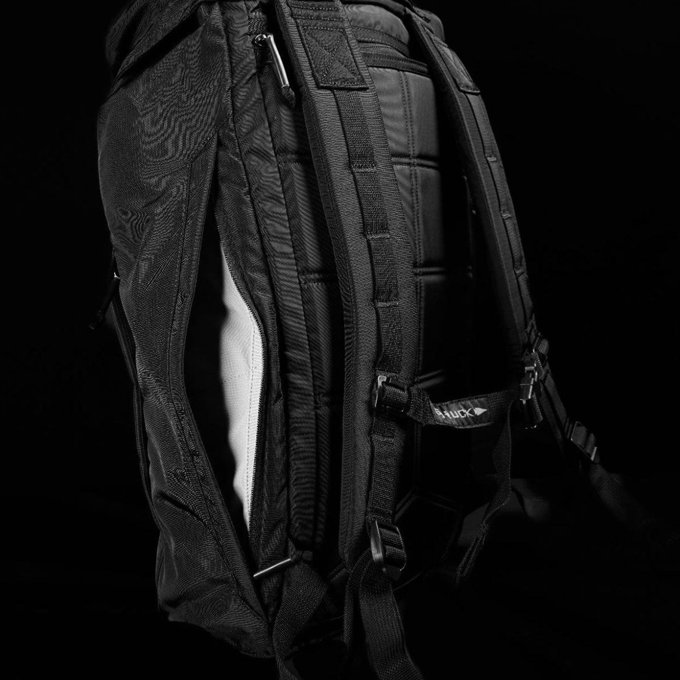 Black backpack with padded straps, side zipper, and textured fabric, shown against a dark background.