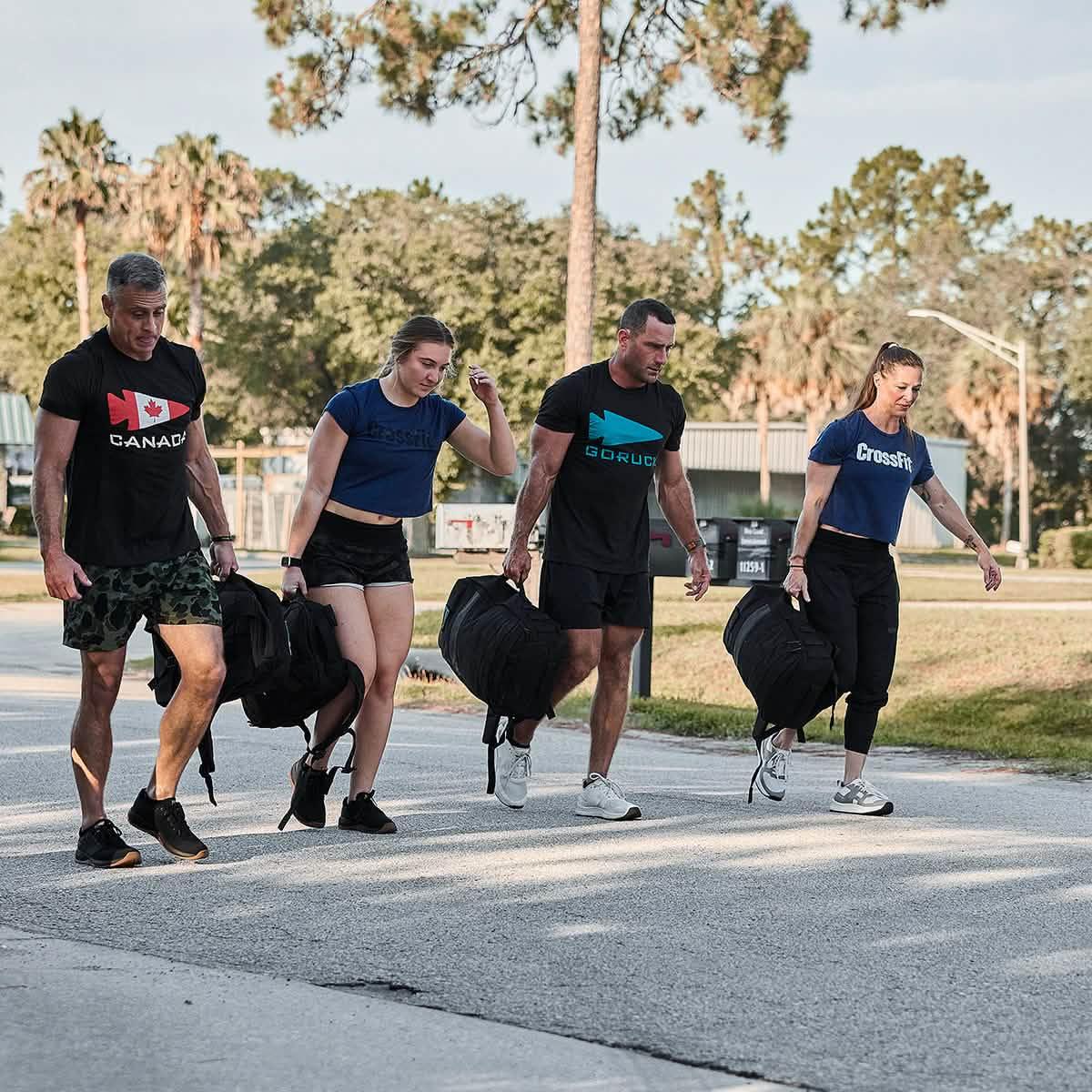 Group of four adults rucking outdoors carrying heavy rucksacks wearing athletic gear and GORUCK t-shirts