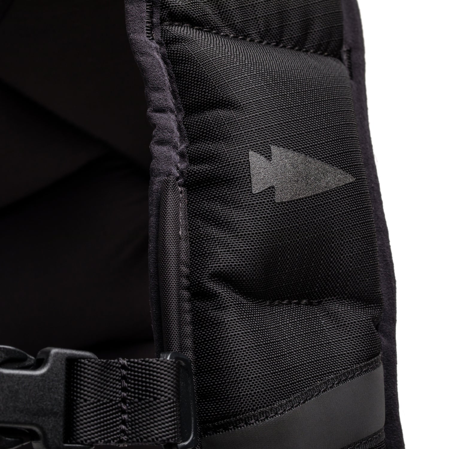 Close-up of a black padded strap with a plastic buckle and arrow-shaped reflective patch, designed for women’s fitness gear or as an accessory for your weighted vest or the Spy Ruck.