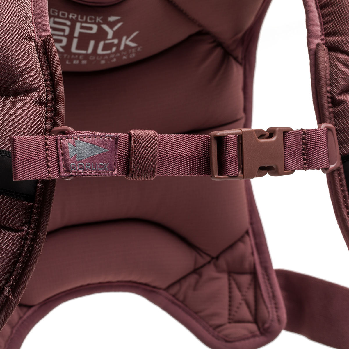 Close-up of a maroon Spy Ruck backpack strap with a plastic buckle and prominent GORUCK branding, showcasing the premium details found in women’s fitness gear.
