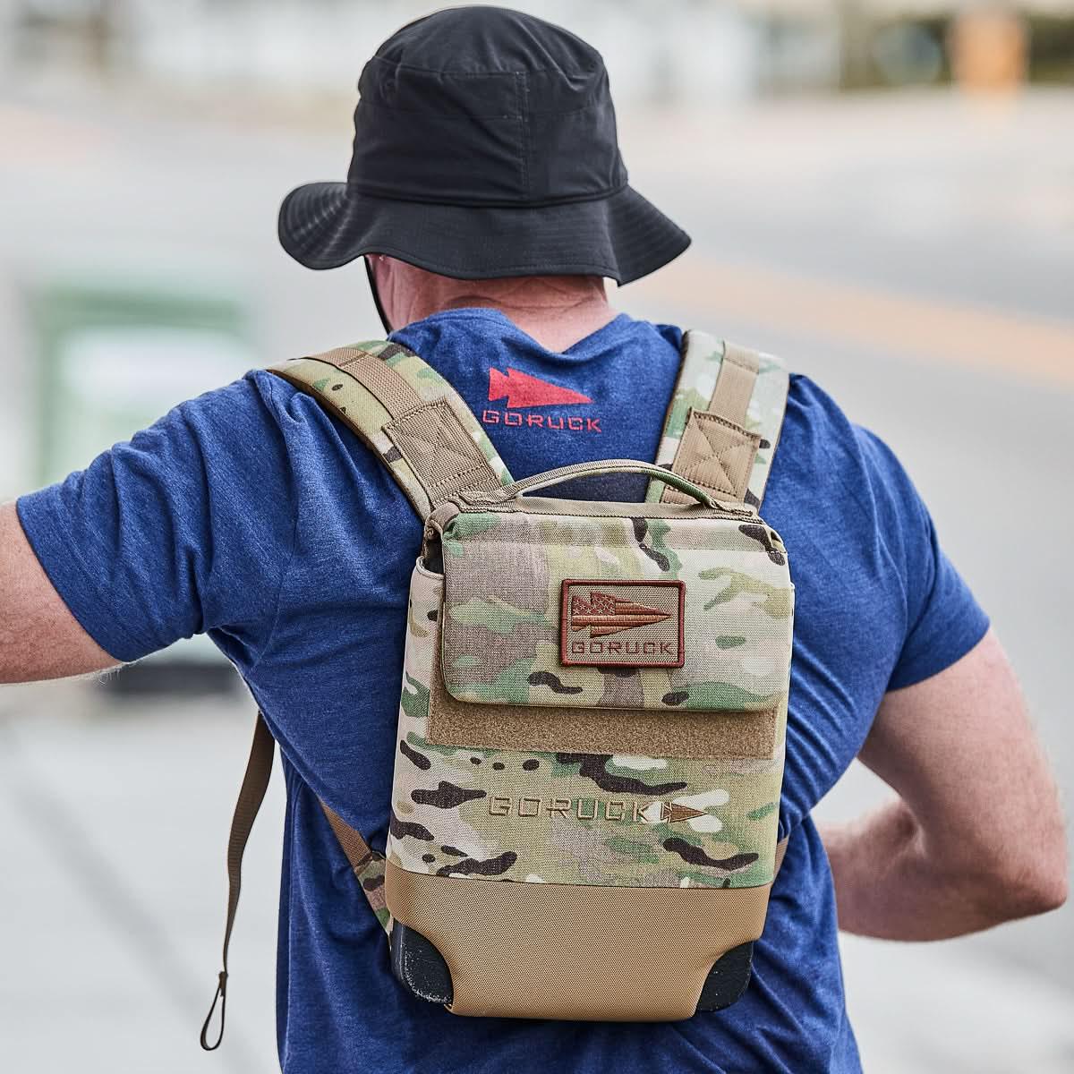 Man wearing navy GORUCK t-shirt and black hat with camo GORUCK backpack outdoors
