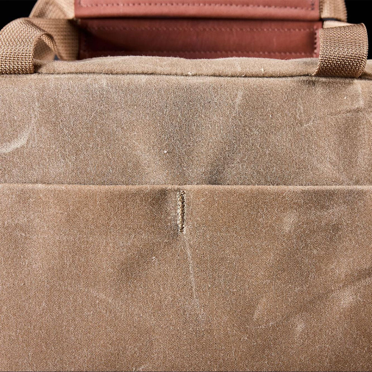 Close-up of a dusty brown canvas bag with tan straps and visible stitching on the fabric.