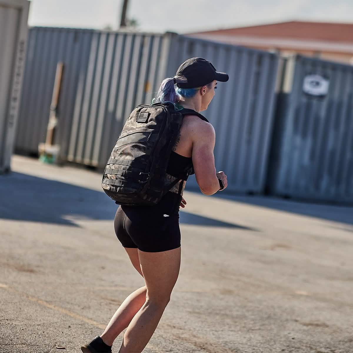 Athlete running outdoors wearing GORUCK tactical black pack and black athletic gear near shipping containers